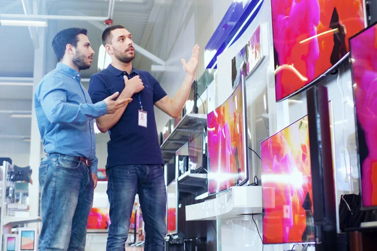 Formation vendeur en magasin Un vendeur professionnel montre les derniers téléviseurs 4K UHD à un jeune homme.